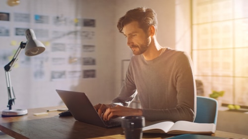 Professional Creative Man Sitting at His Desk in Home Office Studio Working on a Laptop