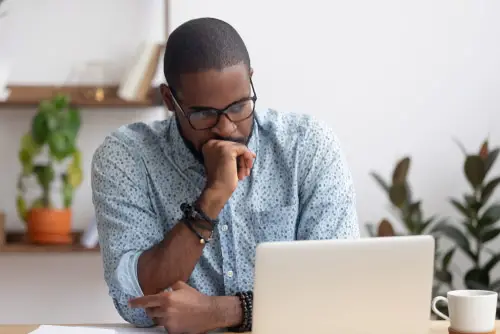 Head shot serious puzzled African American businessman looking at laptop screen sitting in office