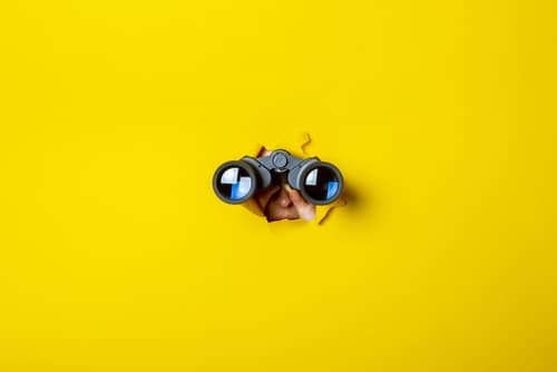 Female hand holds black binoculars on a yellow background