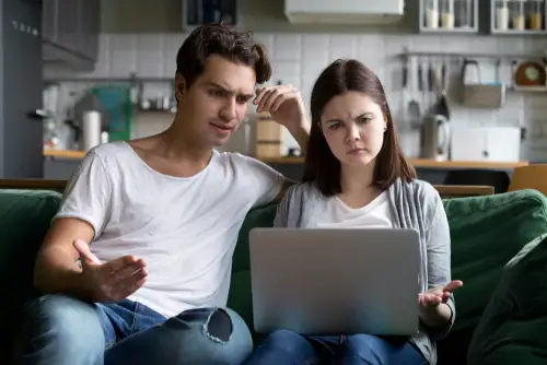 Millennial couple annoyed by stuck laptop sitting together on sofa