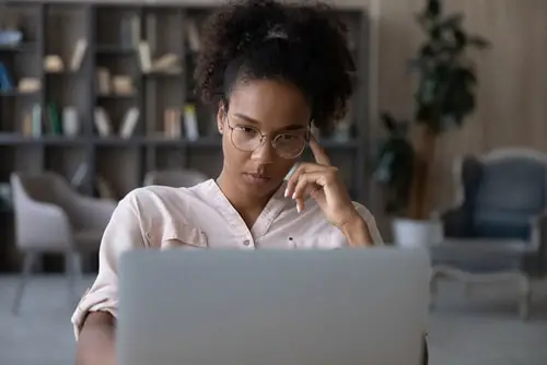 Pensive young biracial woman in glasses look at laptop screen 