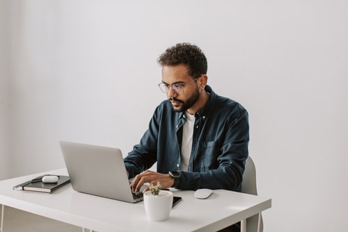 Portrait of young serious black businessman in glasses working at laptop in the office