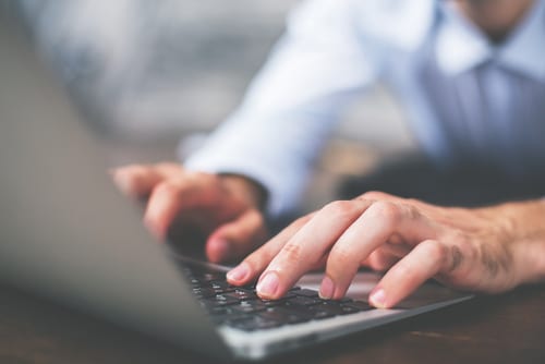 Side view of male hands typing on laptop keyboard