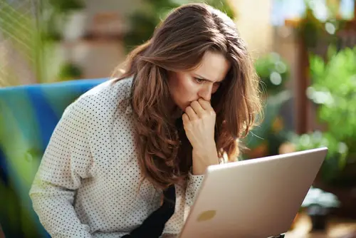 Stressed woman at modern home in sunny day using laptop