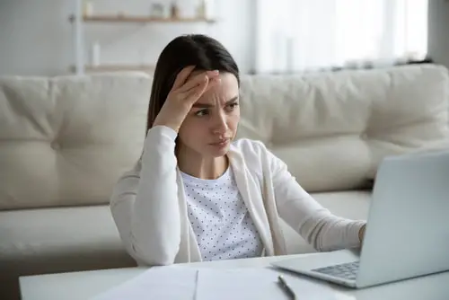 Unhappy young woman sit at home work on laptop